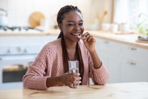Cheerful Young African American Lady Taking Beauty Supplement Pill In Kitchen